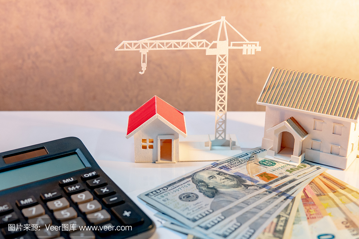 房地产或房地产开发。建设企业投资理念。住房抵押贷款利率。在桌子上有计算器的国际钞票的房子和起重机模型。